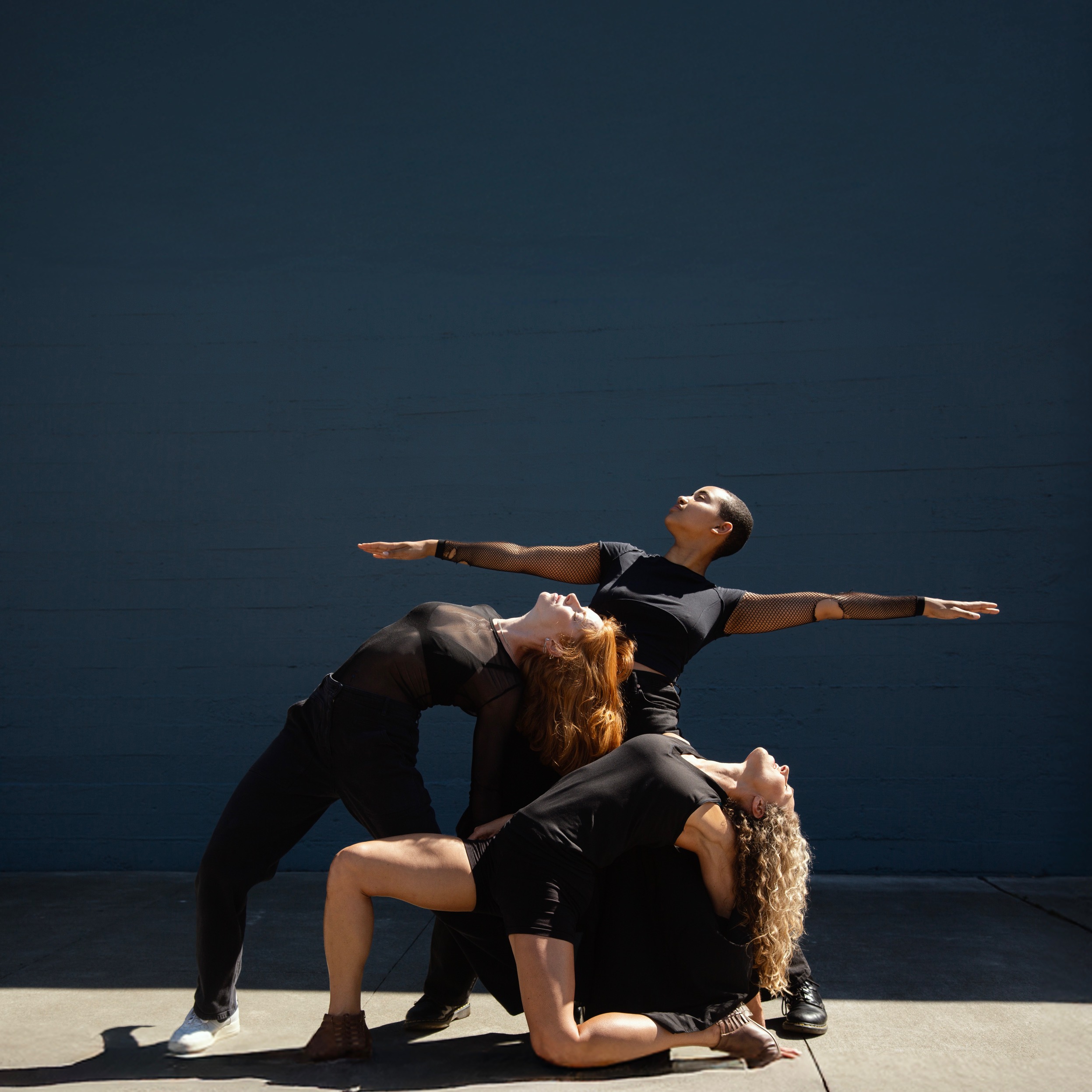 This is a photo of three dancers wearing back clothing looking upwards