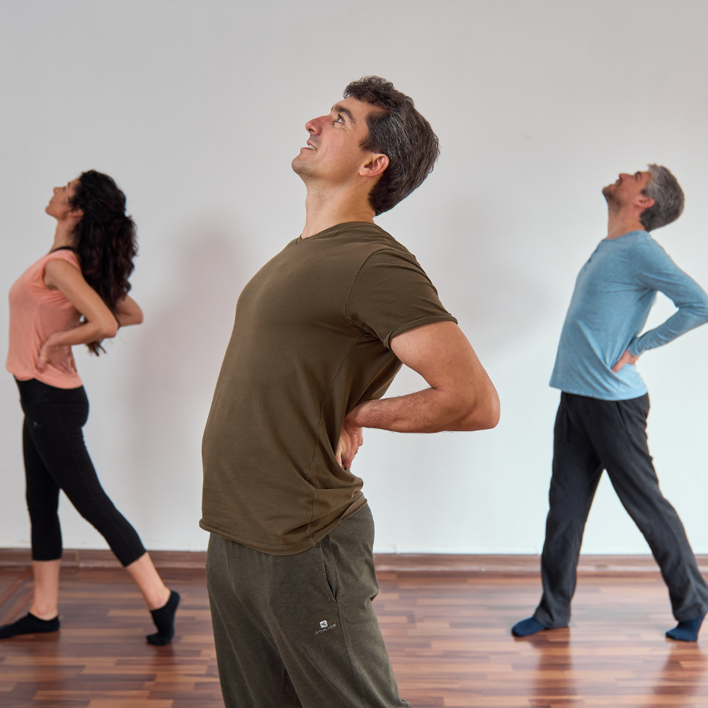 A group of people standing one foot in front of the other with their on their kidneys arching backwards and looking up.
