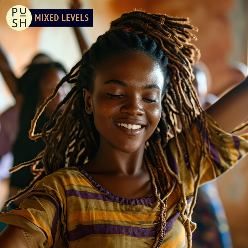 A smiling dancer with their eyes closed dances in a studio filled with warm light, with other dancers visible behind them in a blurred background.