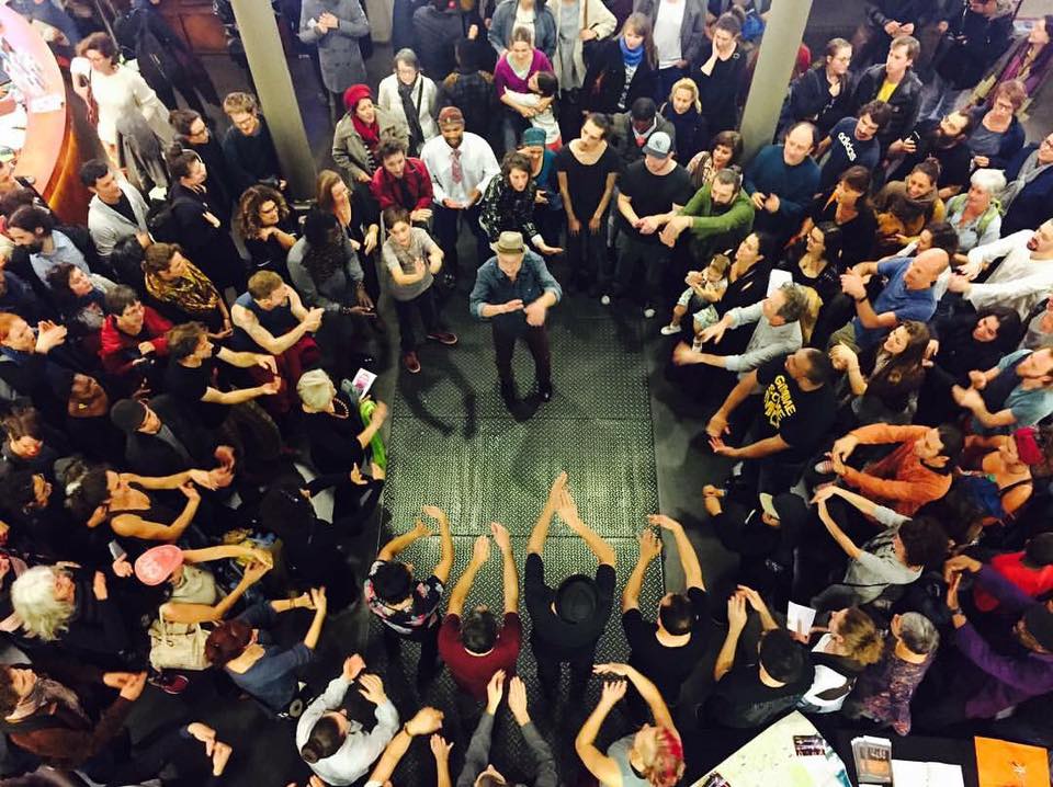 Man in the center of a crowd all clapping, singing