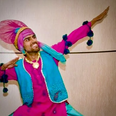 Bhangra dance teacher in traditional Punjabi folk outfit holding a pose and smiling while looking up