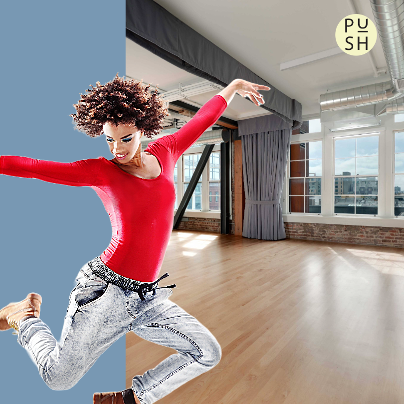 A dancer with an afro in a bright red leotard and drawstring gray pants jumps into the air energetically with arms outstretched and legs bent in the foreground. The background is a split screen with a beautifully sunlit wood floor dance studio on the right, and a bluish-gray background on the left.