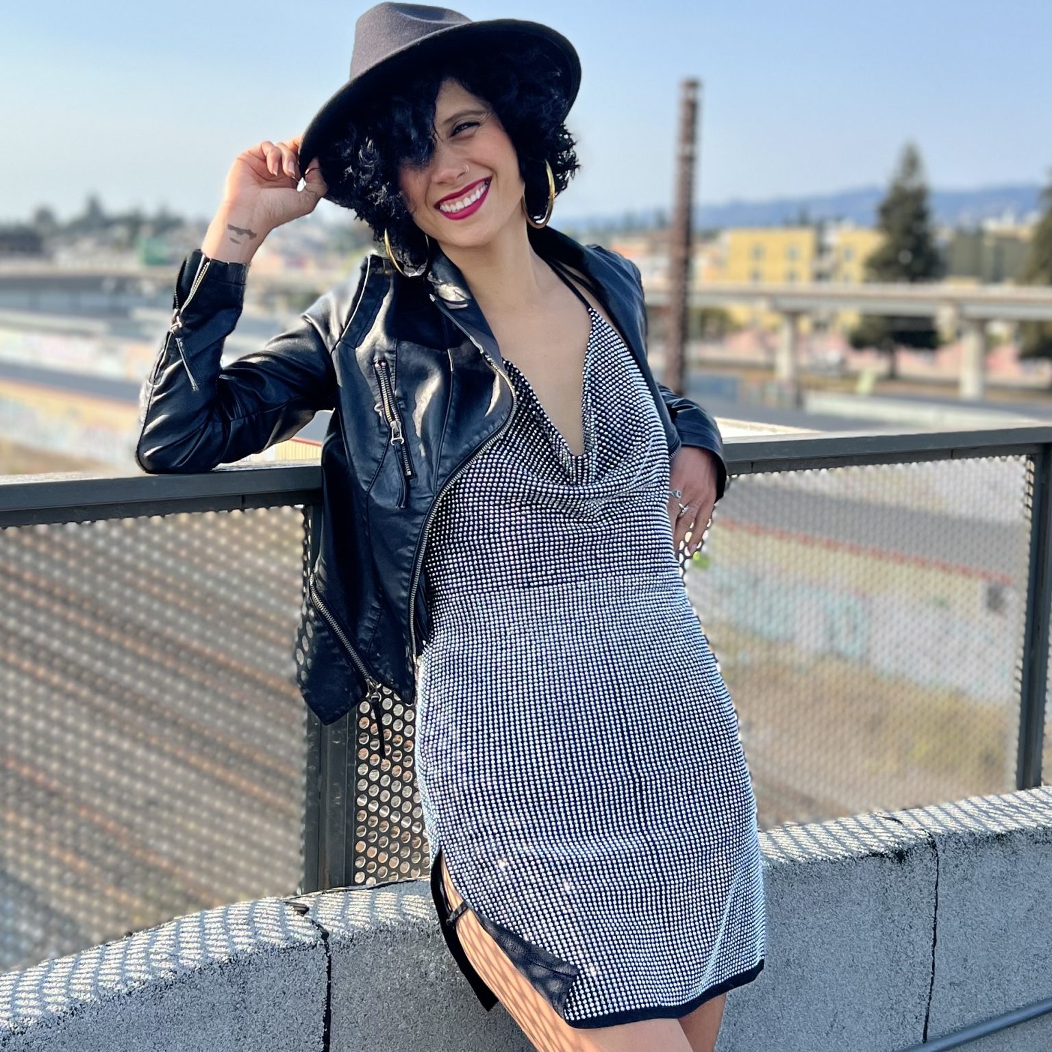 Teacher Aimee Rose stands smiling at the camera in a silver dress and a big-brimmed black hat.