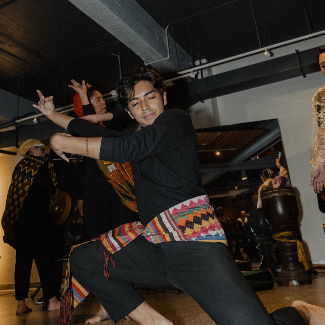 Jan, who is wearing a black turtleneck with a colorful cloth around his waist, is in a pangalay pose.