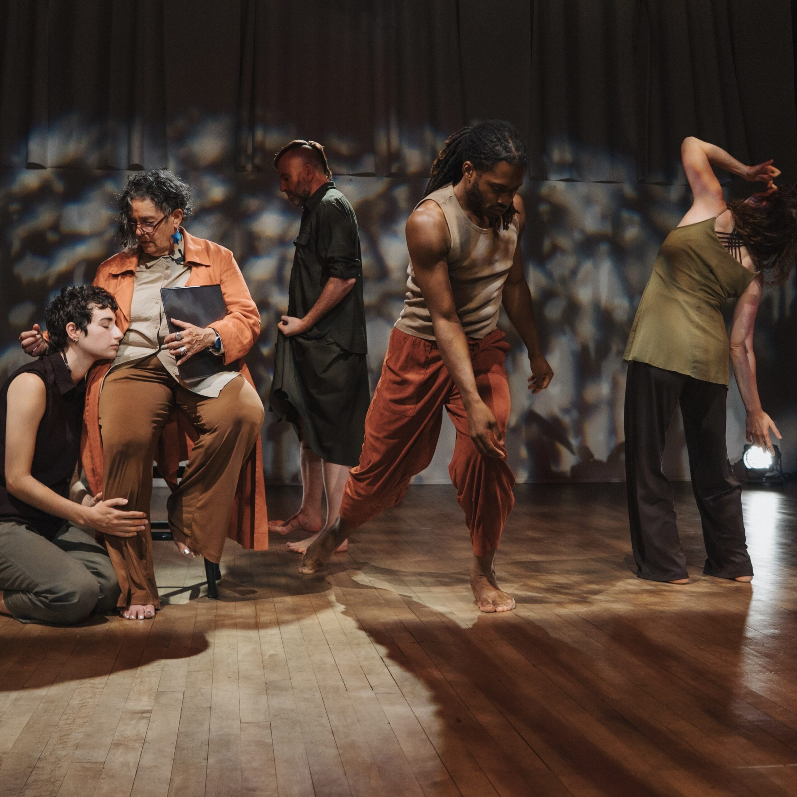 Five dancers pose facing different directions, including one dancer seated in a chair.
