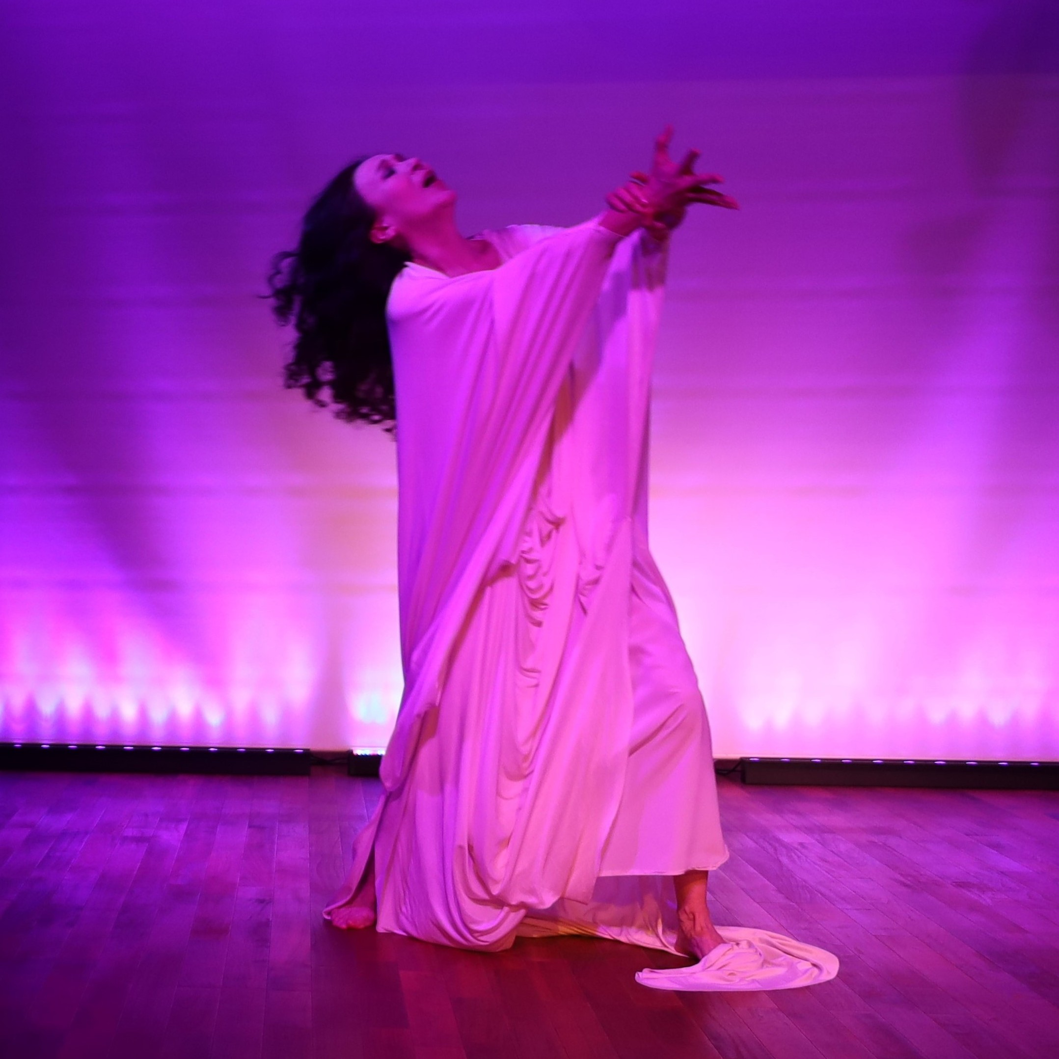 Mary Sano performing dance piece from Tristan and Isolde by Richard Wagner wearing white drapped costume with tragedic/dramatic gesture. 