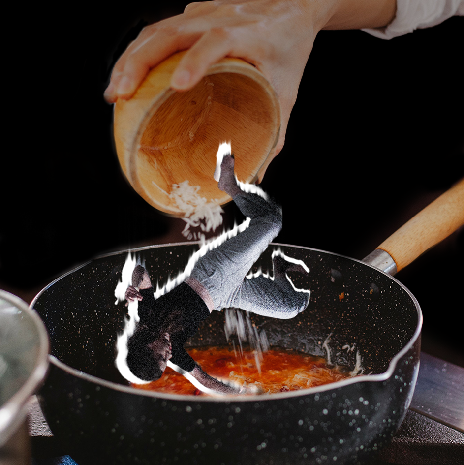 Hand pouring shredded cheese, along with a small upside down person, from a wooden bowl into a black pot of red liquid.