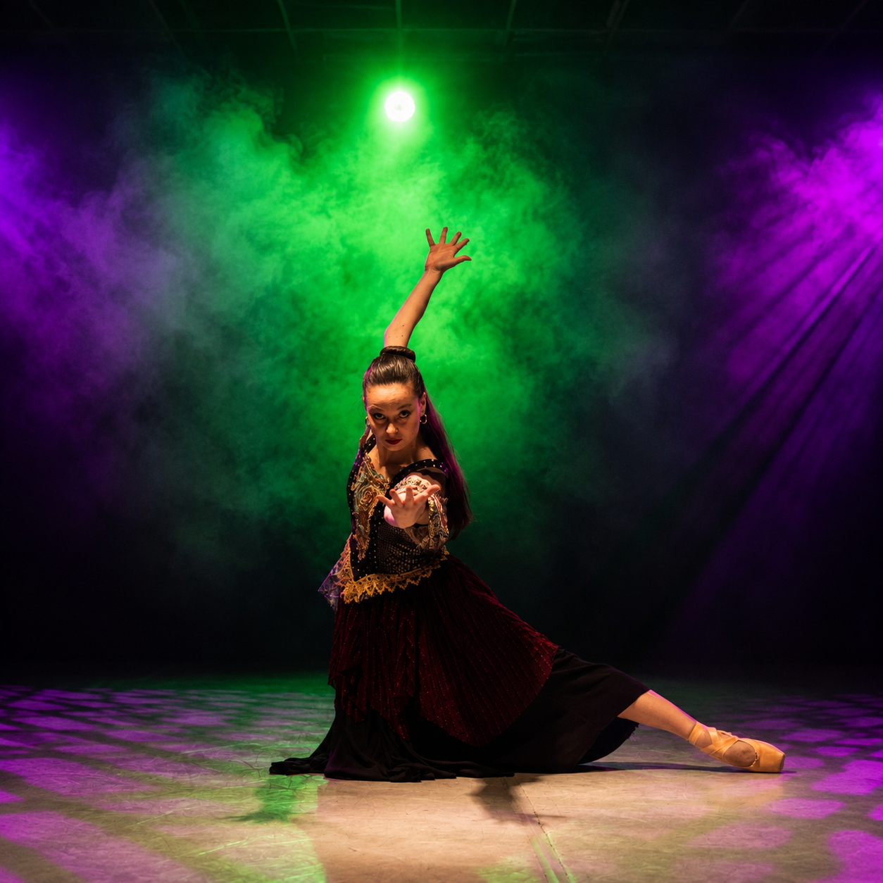 A ballet dancer in an ornate black and burgundy costume holds a dramatic low pose, one arm reaching toward the audience and the other extended overhead. Green and purple lights shine through theatrical fog behind her as her pointed foot stretches to the side.