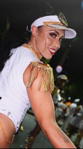 Close up photo of person wearing a white and gold visor and white top with brunette hair looking over their should and smiling