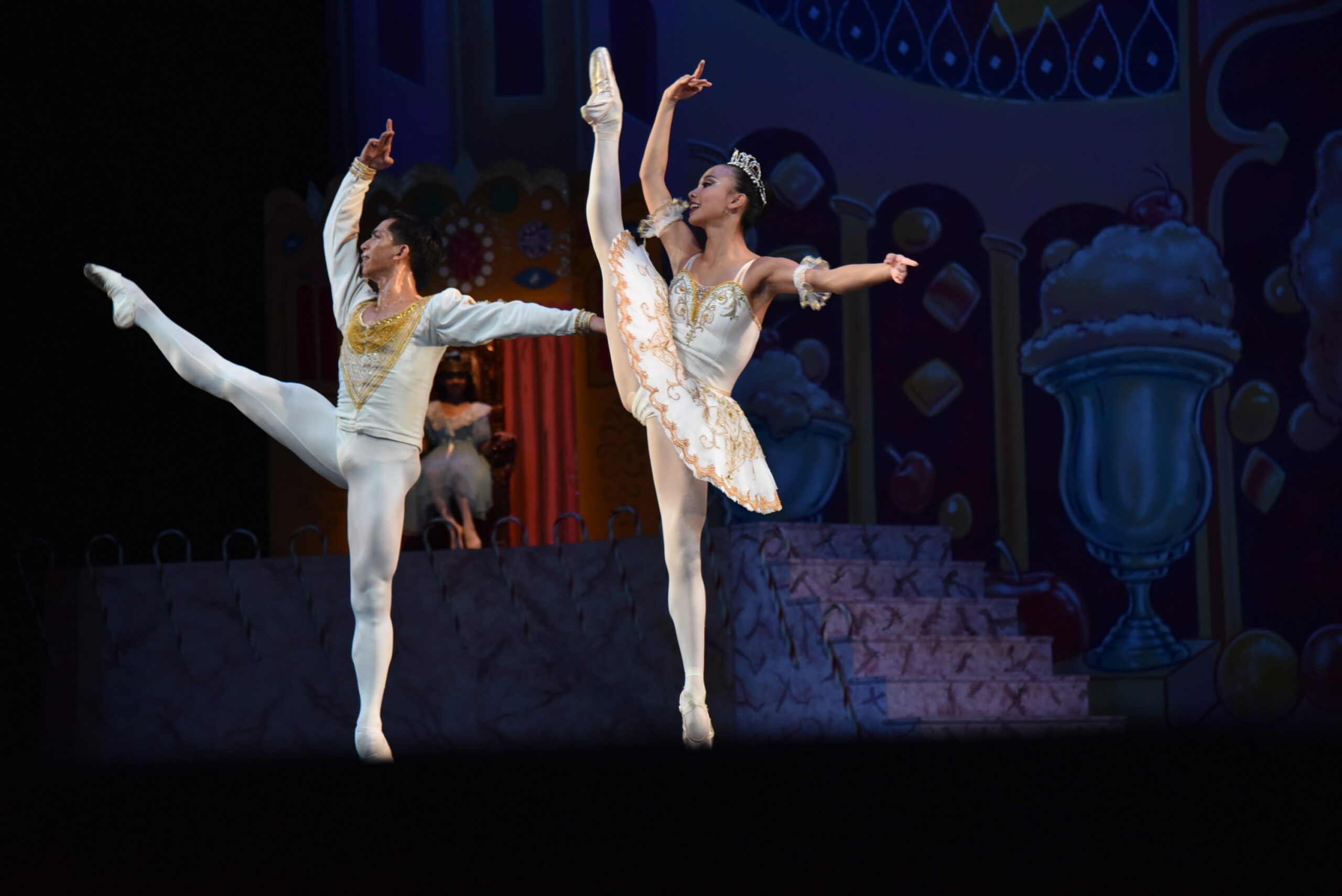 Sugar Plum Fairy and her cavalier caught in a step with their leg up in a developé during a coda of the grand pas de deux